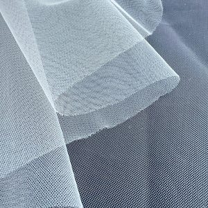 May include: Close-up of white tulle fabric with a fine mesh texture. The fabric is layered, creating depth and shadows. The background is a darker shade of blue, providing contrast to the delicate, sheer material.