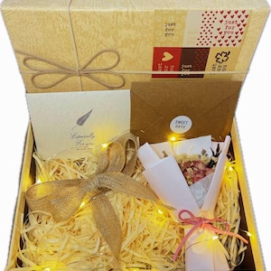 May include: A gift box with a textured beige lid featuring a bow and a label with the text just for you. Inside, the box contains a card with the text Especially For you, a brown envelope with a sticker reading SWEET DAYS, and a small dried flower bouquet.