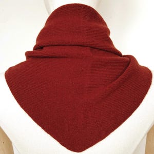 May include: A deep red, triangular-shaped knit scarf with a fine ribbed texture. The scarf is draped around the neck area, featuring a pointed front section that hangs down, showcasing a consistent dark crimson color throughout the entire garment.