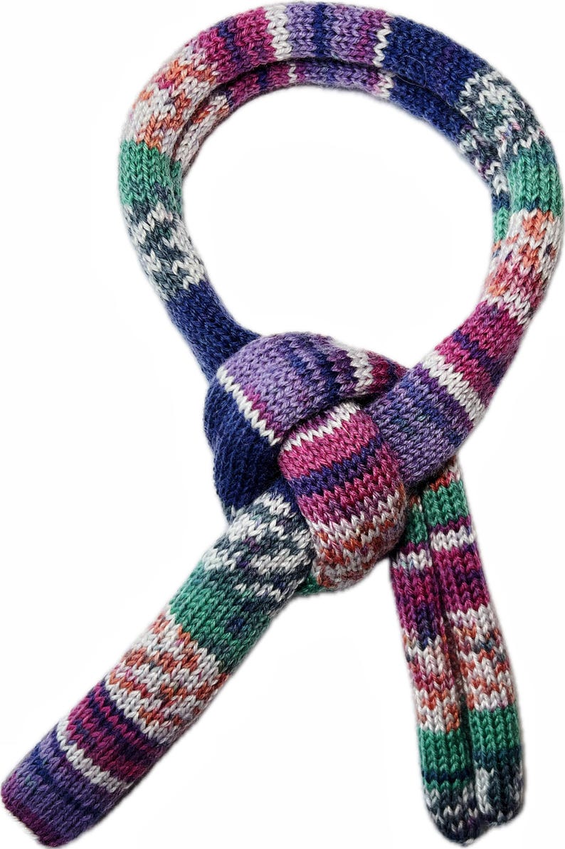 May include: A colorful knitted scarf with a knotted design. The scarf features a mix of colors including blue, purple, green, pink, and white. The scarf is made of a soft, textured material.