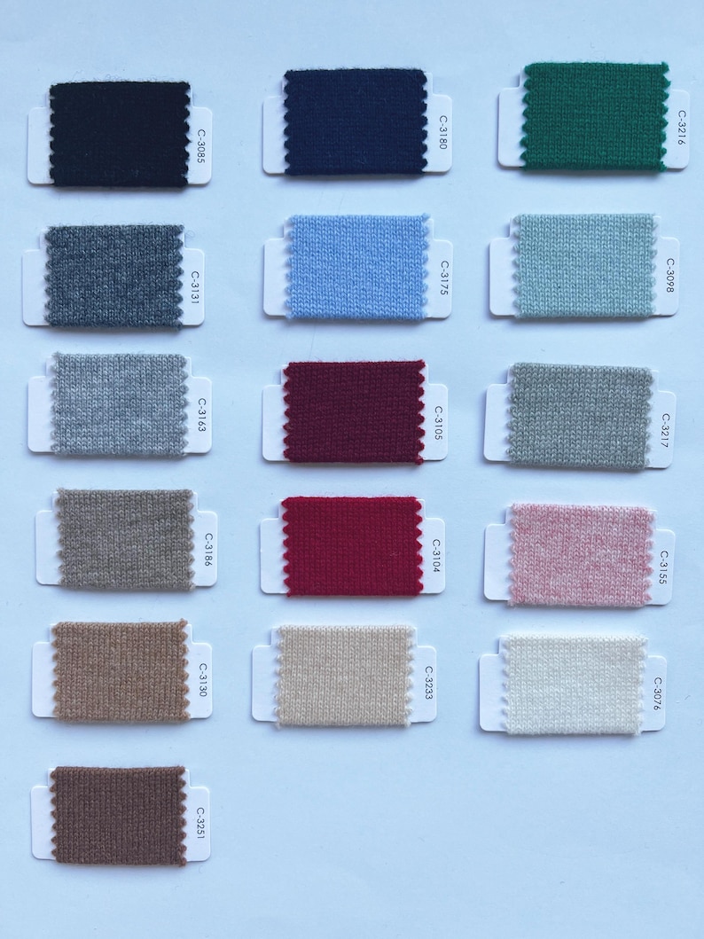 May include: A collection of sixteen rectangular fabric swatches arranged in a grid, each attached to a white card with a scalloped edge. The swatches feature various solid colors including black, navy, green, gray, blue, red, pink, beige, and brown.