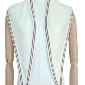 May include: A triangular scarf in off-white knit fabric featuring a double-line border in a light brown tone. The scarf is draped symmetrically, showcasing the clean edges and the consistent color contrast between the cream base and the brown trim.