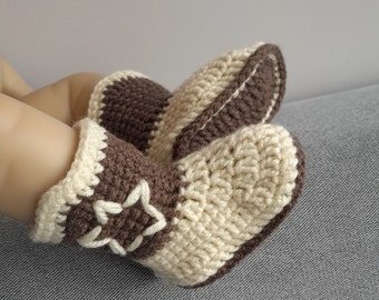 Op de afbeelding: Een paar gehaakte babyschoentjes in bruin en crème met een stervormig ontwerp. De schoentjes zijn gemaakt van zacht garen en hebben een comfortabele pasvorm.