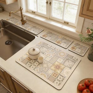 Op de afbeelding: Een aanrechtset met een patroon in beige, grijs en geel. De set bevat een grote mat, twee kleinere matten en een lange mat, plus een kleine kom en een kopje. De matten hebben een tegelachtig patroon.