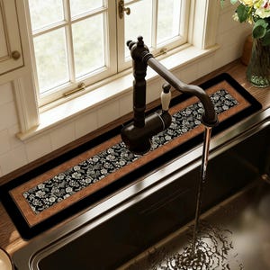 May include: A rectangular kitchen sink mat with a floral design. The mat features a black border, a brown center, and a black and white floral pattern. The mat is placed in front of a kitchen sink and under a faucet.