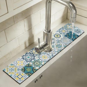 May include: A decorative sink faucet mat with a colorful tile pattern in shades of blue, yellow, and white. The mat is rectangular and designed to sit behind a stainless steel faucet, protecting the countertop from water stains.