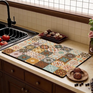 May include: A rectangular kitchen mat with a colourful patchwork tile design. The mat features geometric patterns in orange, blue, brown, and beige. It is placed on a white countertop near a sink.