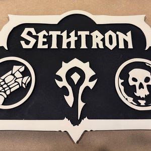 May include: A wooden sign with the name "SETHRON" in bold white letters. The sign features three circular emblems and a decorative border. The central emblem is a stylized symbol, with a skull on the right and a weapon on the left.