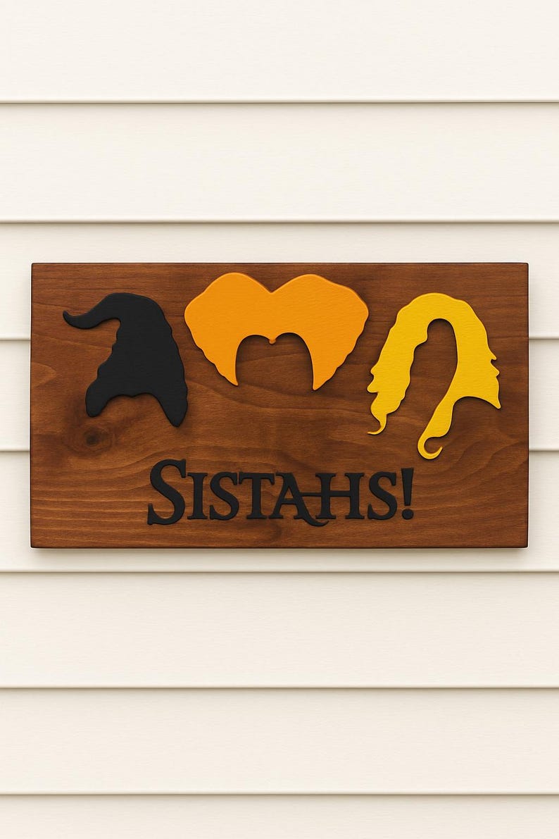 Puede incluir: Letrero de madera con la palabra "SISTAH'S!" y siluetas de un sombrero de bruja, pelo naranja y pelo amarillo. El letrero est&aacute; montado sobre un fondo de revestimiento blanco. Decoraci&oacute;n de Halloween.