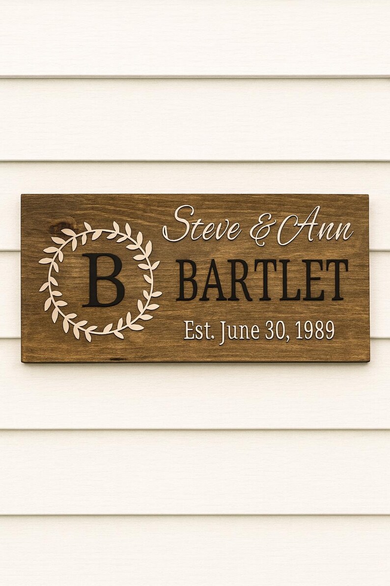 Puede incluir: Letrero de madera rectangular con los nombres "Steve & Ann BARTLET" y la fecha "Est. June 30, 1989". El letrero tiene un fondo marr&oacute;n oscuro con letras blancas y una corona decorativa alrededor de la letra "B".