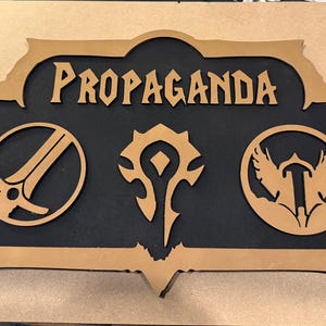 May include: A wooden sign with the word "PROPAGANDA" in a stylized font. The sign features three symbols and a black background, framed by a light brown border. The symbols are a sword, a stylized symbol, and a bird.