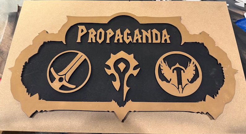 May include: A wooden sign with the word "PROPAGANDA" in a stylized font. The sign features three symbols and a black background, framed by a light brown border. The symbols are a sword, a stylized symbol, and a bird.