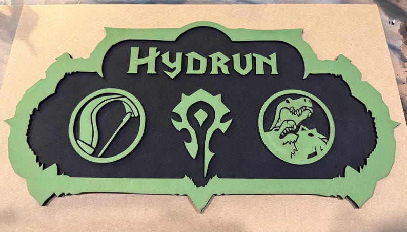 May include: A two-tone wooden sign with the name "HYDRUN" in green lettering. The sign features three green symbols on a black background, including a scythe, a stylized emblem, and a wolf-like creature.