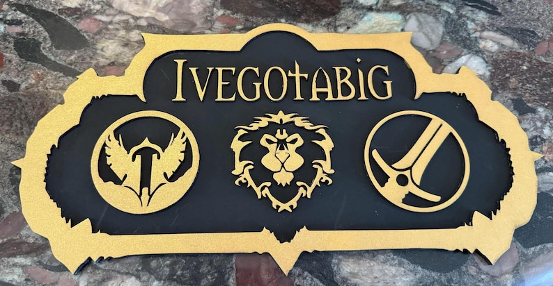 May include: A wooden sign with the text "IVEGOTABIG" in gold lettering. The sign has a black background and features three gold-colored emblems: a bird, a lion's head, and a crossed sword and shield.
