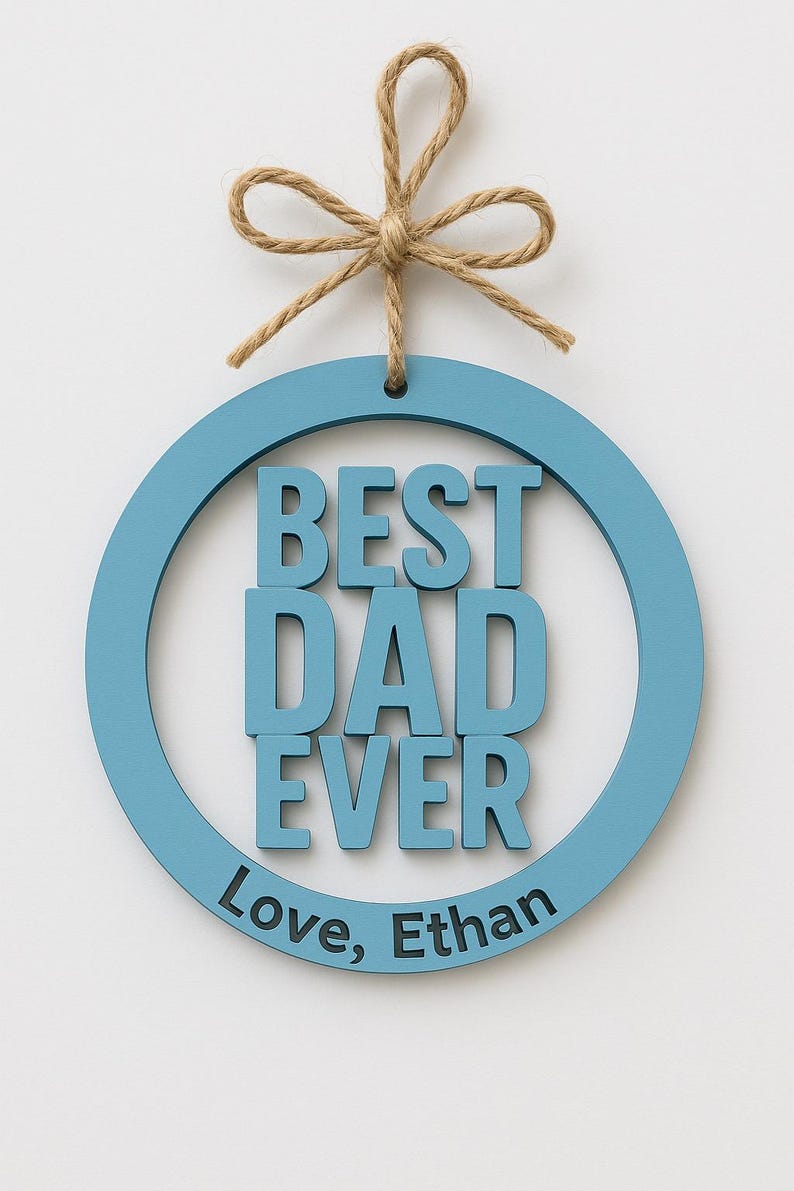 May include: A round, light blue wooden sign with the words "BEST DAD EVER" in bold, raised letters. The sign includes the inscription "Love, Ethan" and is suspended by a natural twine bow.
