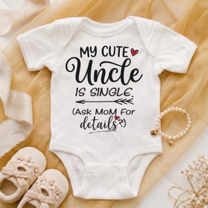 May include: A white short-sleeved baby bodysuit featuring black text that reads MY CUTE Uncle IS SINGLE. (Ask MOM For details?) with two small red hearts and a horizontal arrow graphic printed on the front center of the garment.
