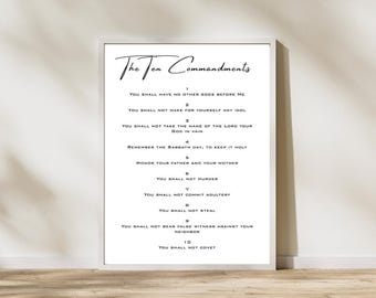 May include: A framed print displaying "The Ten Commandments" in elegant script. The white background contrasts with the black text, listing the commandments in a clear, readable format. The frame is white, and the print is displayed against a neutral wall.