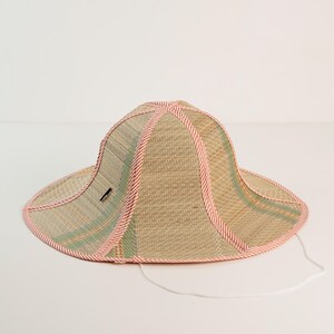 Natural straw hat with red trim, offering a wide brim for shade. Breathable and eco-friendly, it blends rustic charm with modern practicality.