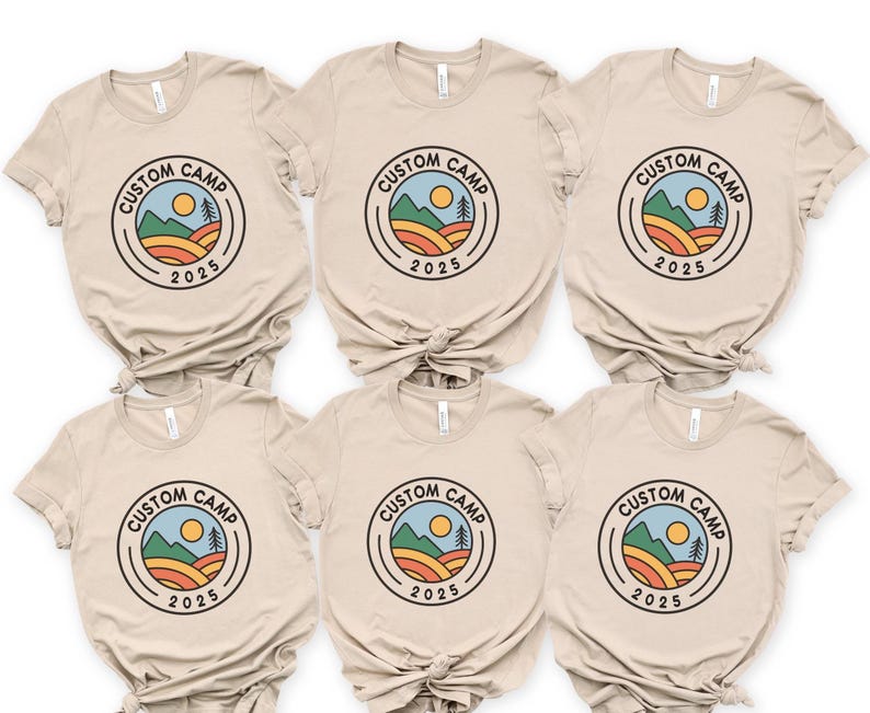 A collection of six beige t-shirts with the same design, featuring a circular logo with a sun, mountains, and text that says "CUSTOM CAMP" and "2025".