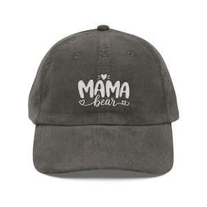 Puede incluir: Gorra de béisbol de pana verde oliva. La gorra presenta el texto bordado "MAMA bear" en blanco, con un corazón encima de la palabra "MAMA" y corazones a ambos lados de la palabra "bear".