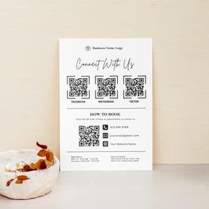 Może przedstawiać: Biała wizytówka z tekstem „Connect With Us” i kodami QR dla Facebooka, Instagrama i TikToka. Zawiera dane kontaktowe i godziny otwarcia. Ozdobna miska z suszonymi liśćmi znajduje się na pierwszym planie.