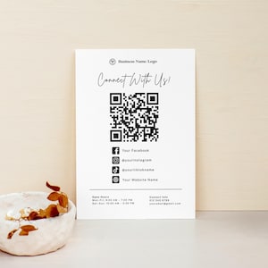 Könnte beinhalten: Eine weiße Visitenkarte mit einem QR-Code und Social-Media-Symbolen. Die Karte lautet "Connect With Us!" und enthält Facebook-, Instagram-, TikTok- und Website-Informationen. Öffnungszeiten und Kontaktinformationen sind ebenfalls aufgeführt. Oben befindet sich ein Logo.