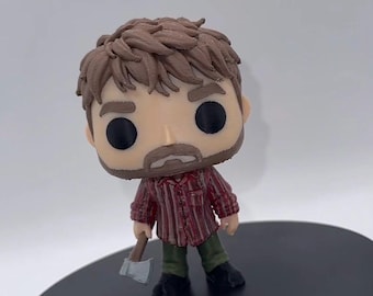 Peut inclure: Une figurine en vinyle stylisée avec des cheveux bruns et une barbe, portant une chemise à manches longues rayée rouge et blanche et un pantalon vert olive. La figurine a de grands yeux noirs circulaires et tient une petite hache grise.