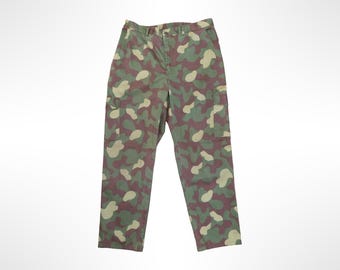 Puede incluir: Pantalones cargo con un patrón de camuflaje en tonos verde oliva, marrón oscuro y beige. Los pantalones incluyen un cierre de botón en la cintura, una cremallera y dos grandes bolsillos cargo laterales situados en los muslos de cada pierna.