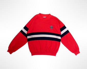 May include: A bright red long-sleeve sweatshirt featuring a mock neck collar and ribbed cuffs. The chest and sleeves are accented with a horizontal stripe pattern in navy blue and white. A small embroidered green crocodile logo is on the chest.