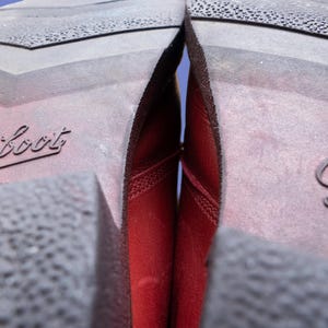 May include: The dark red leather uppers of a pair of boots are visible between the dark brown rubber soles. The soles feature a textured tread pattern and the word Paraboot is embossed on the heel area of each sole in a cursive script font.