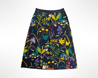 May include: A dark navy blue A-line skirt featuring a vibrant botanical print of various wildflowers, grasses, and leaves in shades of yellow, green, pink, purple, and white. The skirt has a fitted waistband and a side zipper closure.