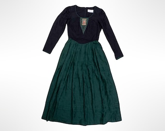 May include: A long-sleeved dress featuring a black bodice with a scoop neckline and a central decorative panel with a small floral pattern. The skirt is a deep forest green with a pleated design and a subtle horizontal band near the hemline.