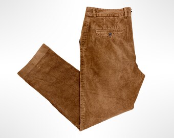 May include: A pair of brown corduroy trousers featuring a textured ribbed fabric, a structured waistband with belt loops, and a single rear pocket with a button closure. The pants are shown folded, displaying the straight leg cut and hem.