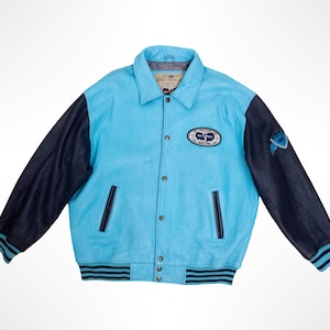Puede incluir: Una chaqueta universitaria de cuero azul claro con mangas azul marino oscuro. La prenda cuenta con cierre frontal de botones, dos bolsillos laterales y puños y dobladillo acanalados a rayas. Incluye un parche ovalado en el pecho izquierdo.