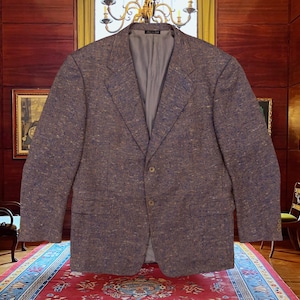 Op de afbeelding: Een bruine tweed blazer met een sluiting met twee knopen en een revers. De jas heeft twee voorzakken en een lichtgrijze voering. De stof heeft een getextureerde uitstraling met blauwe en gouden vlekken. Een klassieke blazer voor diverse gelegenheden.