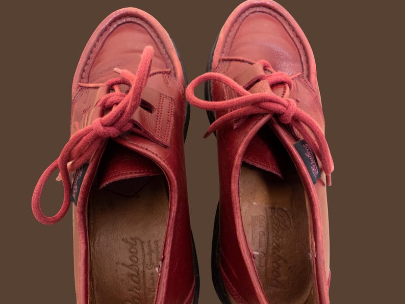 May include: A pair of red leather shoes with matching red laces and a moccasin-style toe construction. The interior insoles feature the embossed Paraboot brand name. The shoes have a dark sole and a small branded fabric tag on the side.