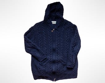May include: A dark navy blue zip-up hoodie featuring a prominent cable knit pattern throughout the body and sleeves. The garment includes a hood, a full-length front zipper with a metal pull, and two front pockets integrated into the knit design.