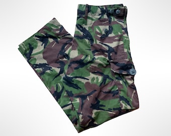 May include: Cargo pants featuring a multi-colored camouflage pattern in shades of green, brown, and black. The pants include a button-up waist closure, a side cargo pocket with a button flap, and a structured waistband with side adjustment tabs.