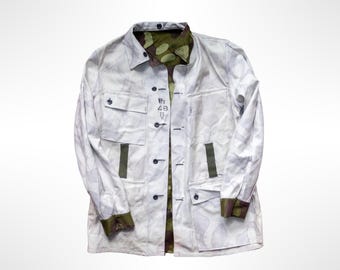 May include: A white jacket with a subtle gray camouflage pattern, featuring a button-down front, a chest pocket, and two lower pockets. The interior lining and cuffs display a green and brown camouflage print. Text reads VPu 48.