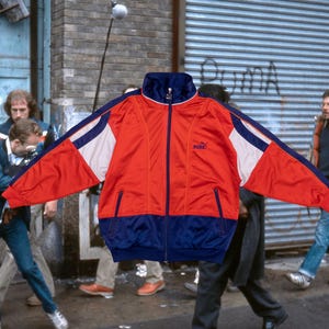 Könnte beinhalten: Vintage Puma Trainingsjacke in Rot, Weiß und Marineblau. Die Jacke hat einen durchgehenden Reißverschluss, Seitentaschen und das Puma-Logo. Die Retro-Jacke hat einen hohen Kragen und Streifen an den Ärmeln.