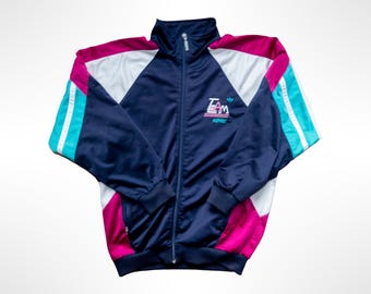 May include: A navy blue zip-up track jacket featuring white and magenta color-blocked panels on the shoulders and sides. The sleeves have bright teal stripes. The chest displays the text "TEAM" in white and magenta with the adidas logo below.