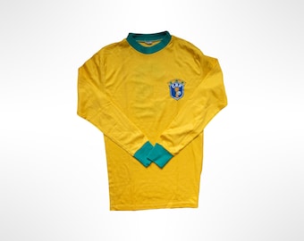 May include: A long-sleeve yellow jersey with a green crew neckline and green cuffs. The chest features a blue and gold shield-shaped emblem with the letters CBF and five small green stars positioned above the shield design.