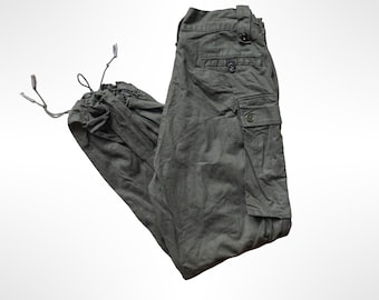 May include: Olive green cargo pants featuring a button-up waist, a side cargo pocket with a button closure, a rear pocket with a button, and adjustable drawstring ties at the bottom of the pant legs for a customizable fit.