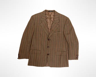 May include: A tan and brown plaid blazer featuring a three-button front closure, notched lapels, two flap pockets at the waist, and three small buttons on each sleeve cuff. The interior is lined with a solid brown fabric.