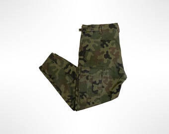 Puede incluir: Pantalones cargo con estampado de camuflaje en tonos verde oliva, marrón y negro. Los pantalones incluyen un bolsillo cargo lateral con cierre de solapa en la pierna y una cintura con correas de ajuste laterales integradas y hebilla metálica.