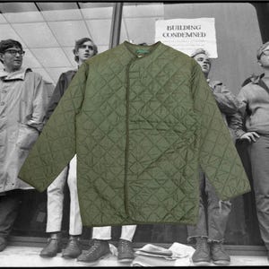 May include: An olive green quilted jacket with a diamond pattern. The jacket has a round collar and long sleeves. The background features a black and white photo of people standing in front of a building with a "BUILDING CONDEMNED" sign.