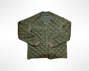 May include: An olive green quilted jacket featuring a V-neckline, long sleeves with ribbed cuffs, and a front opening. The interior label displays the size XL and additional text. The diamond-patterned stitching covers the entire exterior surface.
