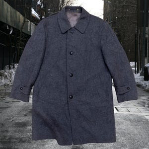 May include: A charcoal gray, knee-length overcoat with a classic collar and button-down closure. The coat features two front pockets and buttoned cuffs. The coat is made of a wool-like material, suitable for cold weather.
