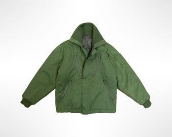 May include: An olive green insulated jacket featuring a high collar, a central front zipper closure, and two diagonal zippered chest pockets. The garment includes long sleeves with ribbed cuffs and a smooth, solid-colored outer shell fabric.