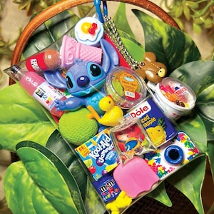 K&ouml;nnte beinhalten: Ein durchsichtiger Kunststoffbeutel mit blauem Karabinerhaken, der verschiedene Miniaturgegenst&auml;nde enth&auml;lt, darunter eine blaue Stitch-Figur, eine gelbe Ente, einen Kool-Aid Jammer-Beutel, eine Dole-Ananasdose, eine kleine Kamera und eine M&M's-T&uuml;te.